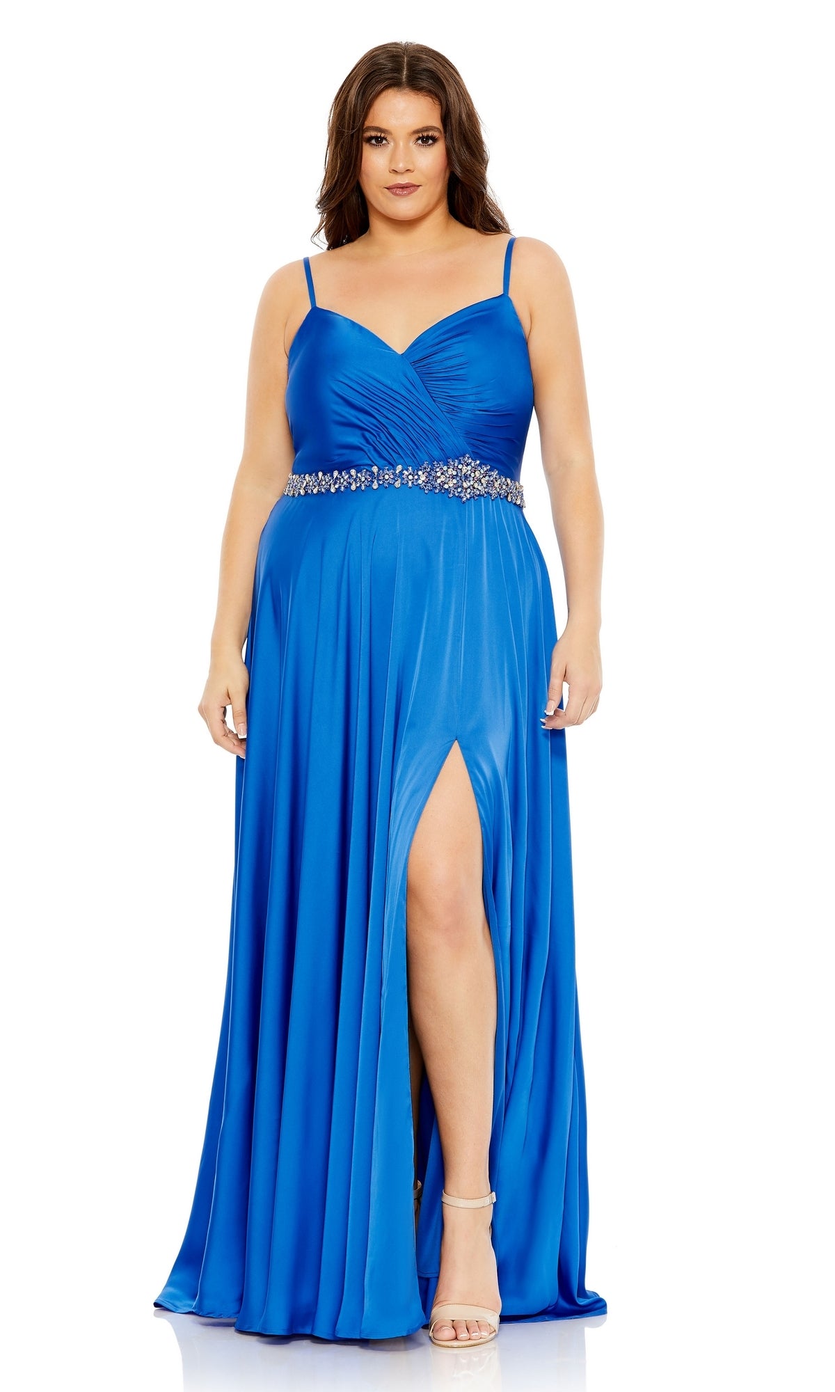 A woman wears the Long Plus-Size Formal Dress 49575 by Mac Duggal, a cobalt blue sleeveless gown with a ruched bodice, embellished waistline, thigh-high slit, and silver sandals.